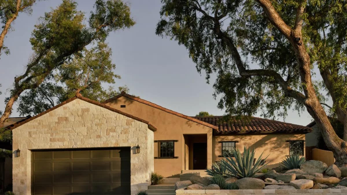 Single-story limestone and stucco single-family rental home with a terracotta tile roof, live oaks and agave xeriscaping on a quiet Stone Oak street at golden hour, the kind of San Antonio property the average rent is measured on