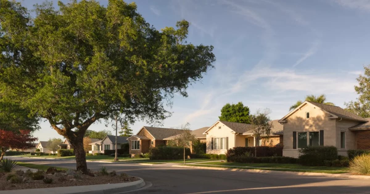Quiet suburban street of single-story limestone and brick single-family homes under mature live oaks at golden hour, the kind of San Antonio-area rental neighborhood investors compare when choosing where to buy