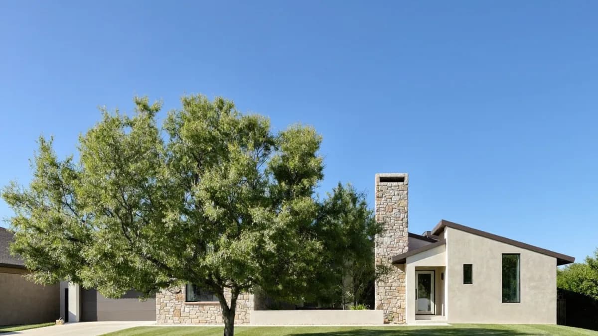 Single-story limestone and stucco home behind a mature shade tree on a mowed lawn under a clear blue sky, the kind of Austin-area house a first-time owner turns into a rental when learning how to become a landlord in Texas
