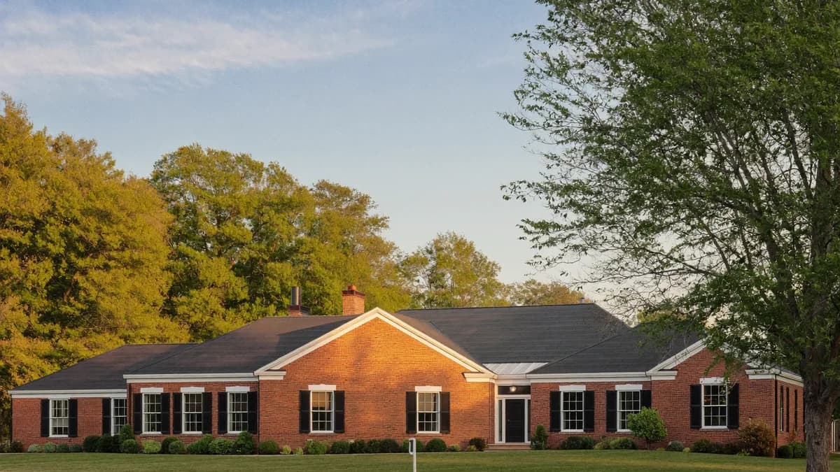 A long red brick single-family rental home with white trim and black shutters, lit by late-afternoon sun with mature trees behind it and a freshly mown lawn in front, the kind of Maryland rental where security deposit law decides who keeps the money at move-out.