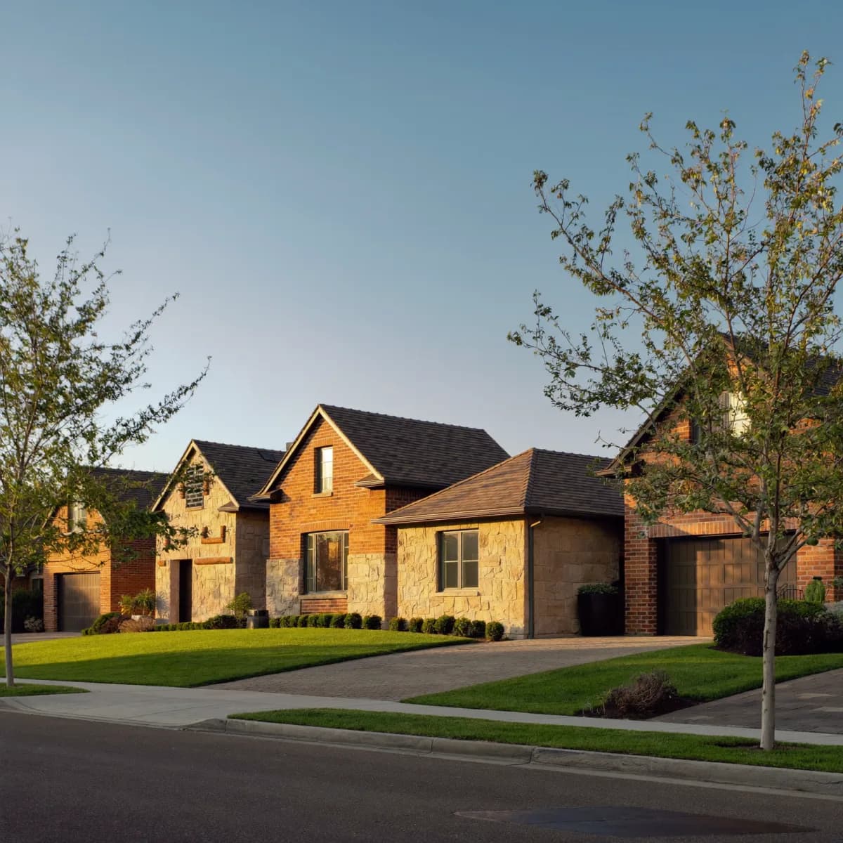 Quiet North Texas suburban street of brick and stone single-family rental homes at golden hour, the kind of Dallas-Fort Worth property governed by Texas landlord-tenant law